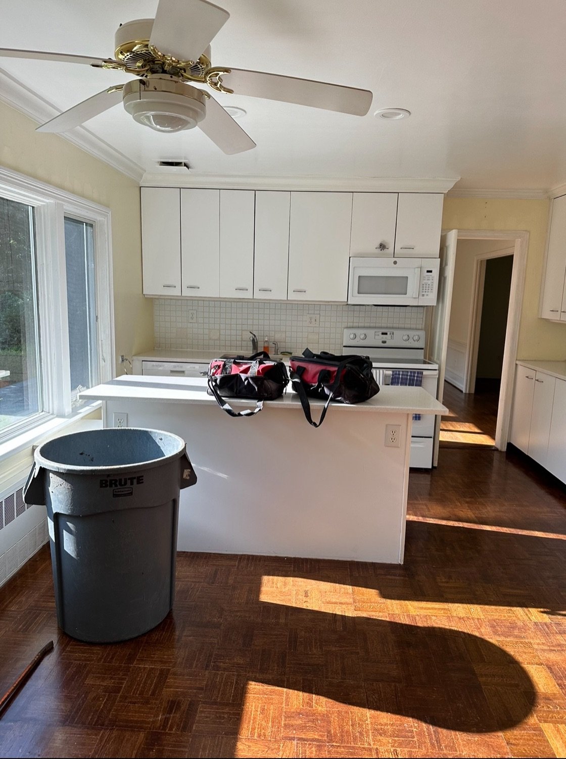 Before — original kitchen with flat white cabinets, white appliances, and parquet flooring