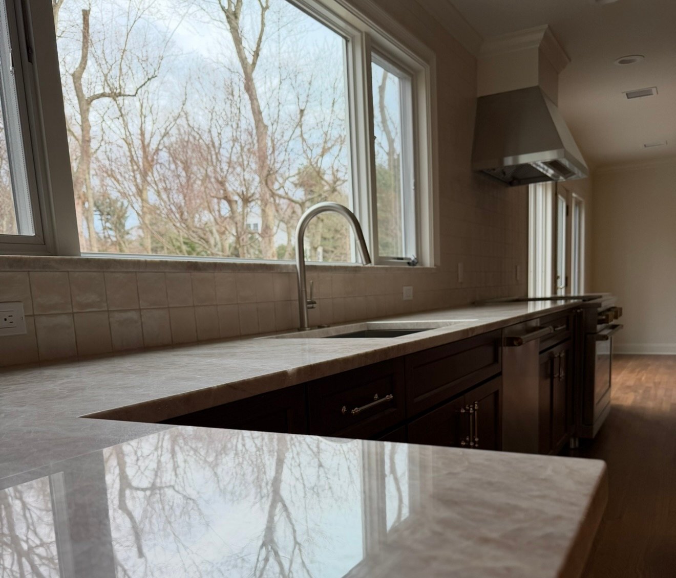 Custom kitchen with marble countertops, stainless faucet, and range hood by a large window